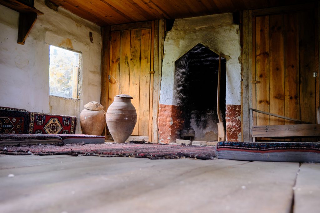 inside the old and abandoned village house made of wooden material and there are large size earthenware jars near the window and antique style carpets and ingle.